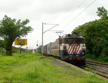 A Ajni WAG-7# 27255 starts entering the lush green atmosphere of Platform 3 of Udvada station with a Jnpt bound container load. 