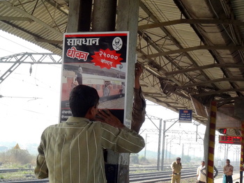 A worker at Kopar station starts attaching poster warning people not to travel on rooftop in Ac power.